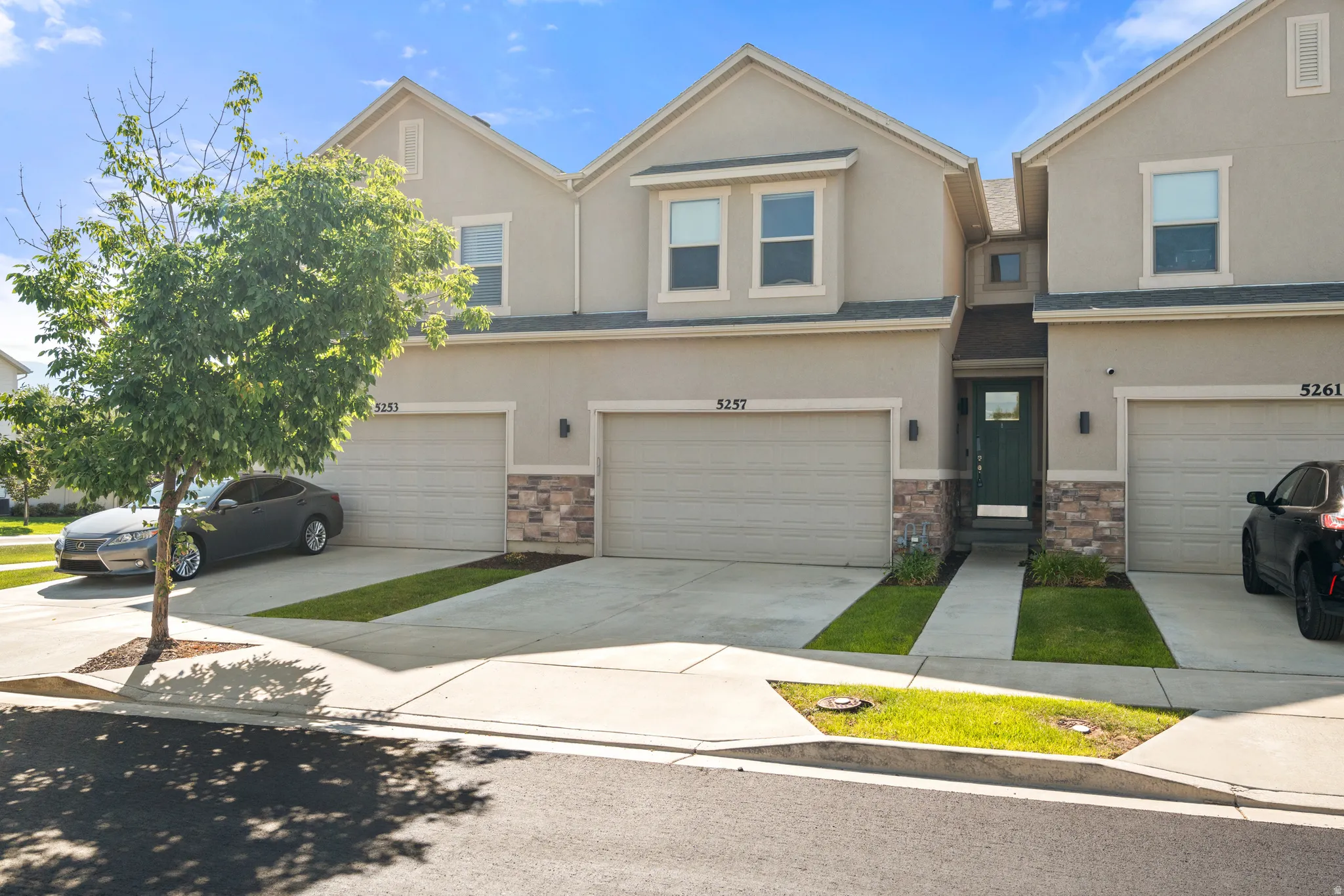 Stucco exterior featuring a dark green front door, stone veneer accents, and two single-car garages