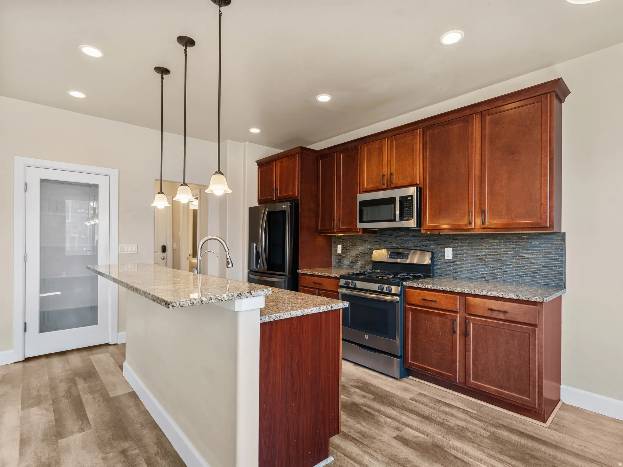 Kitchen featuring wood-finish flooring, recessed lighting, and a granite-topped island with pendant lighting