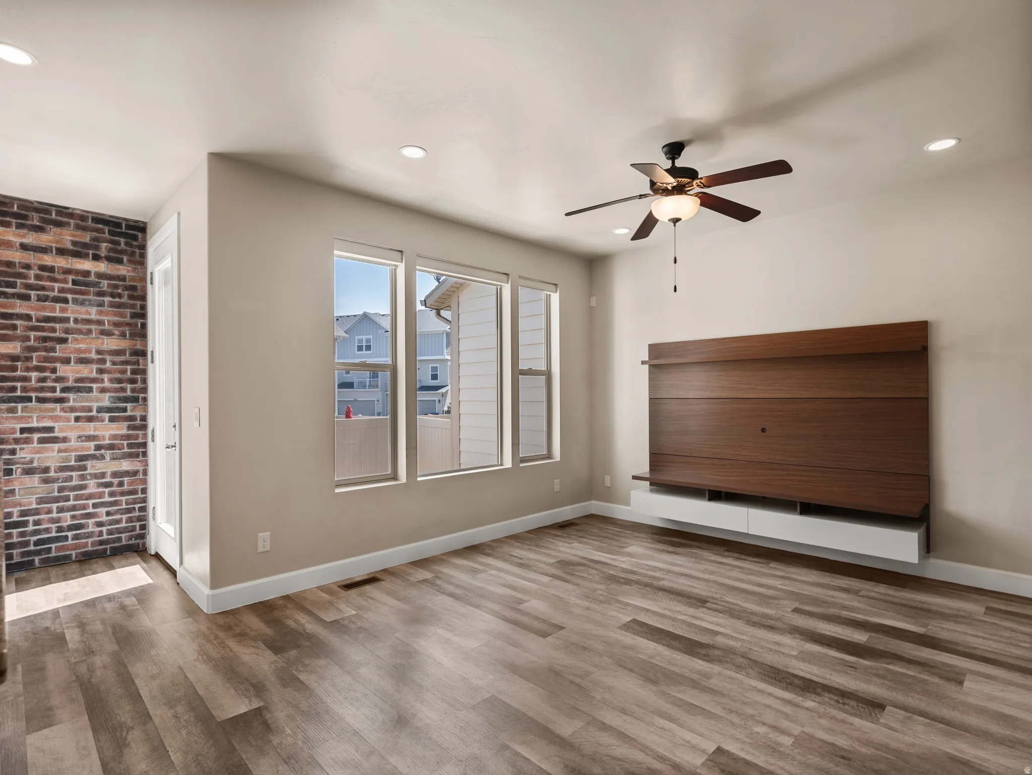 Open-concept space featuring wood-finish flooring, a decorative brick accent wall, and three large windows