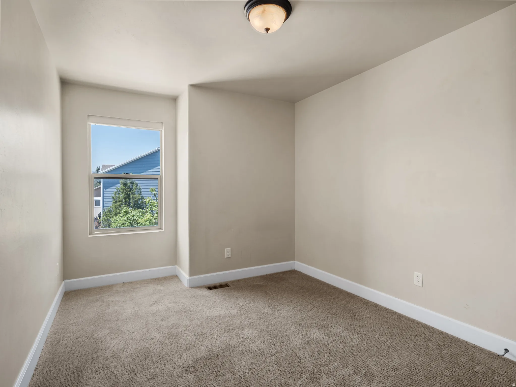 Bright corner bedroom featuring neutral paint finishes, carpet flooring, and abundant natural light from a large window framing mountain scenery