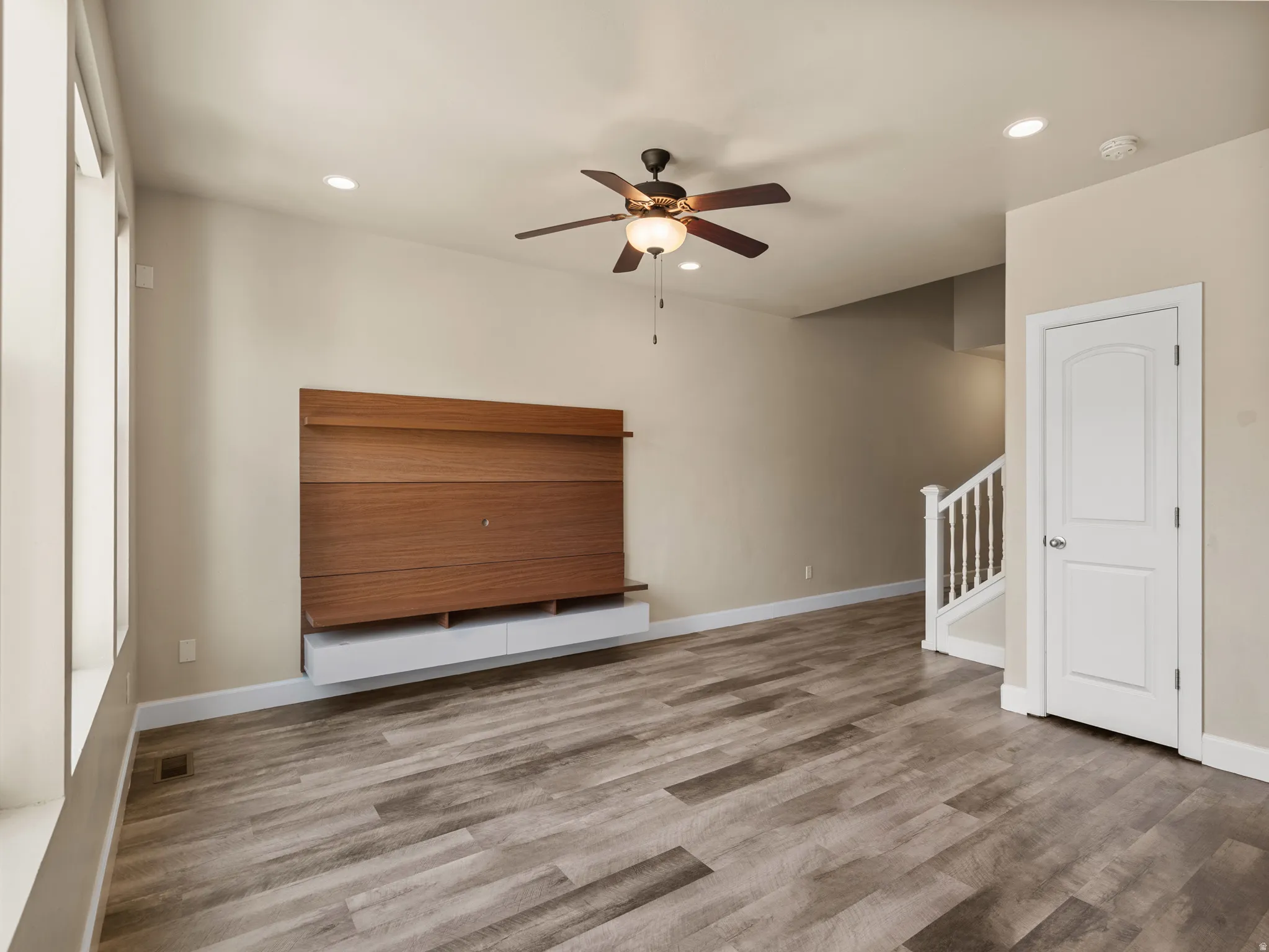 Spacious living area featuring wood-finish flooring, a contemporary built-in media console, and a ceiling fan with integrated lighting