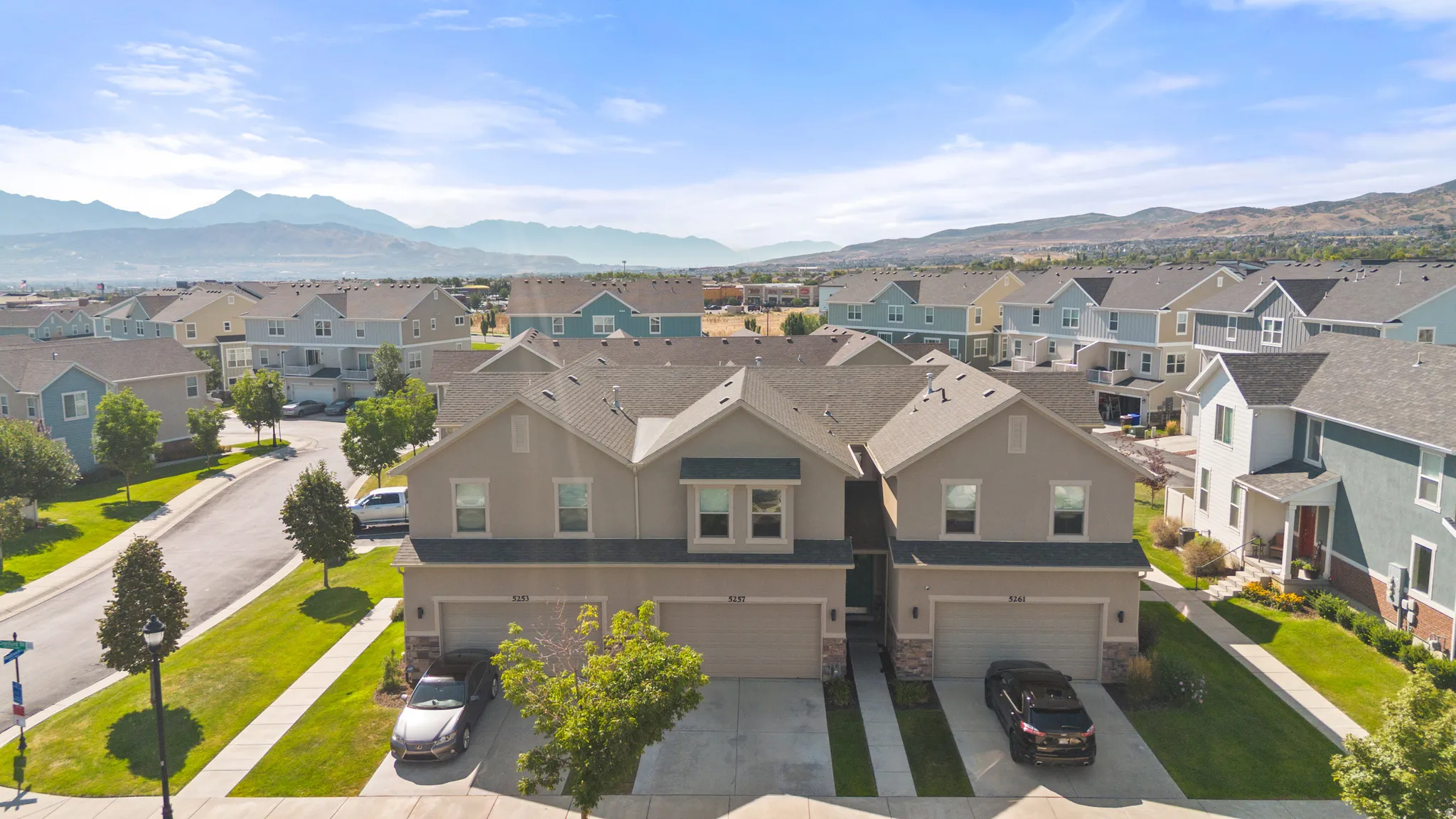 Charming townhome community featuring two-story tan and gray exterior elevations with attached two-car garages, manicured front landscaping with mature trees and established lawn, and mountain vistas in the distance
