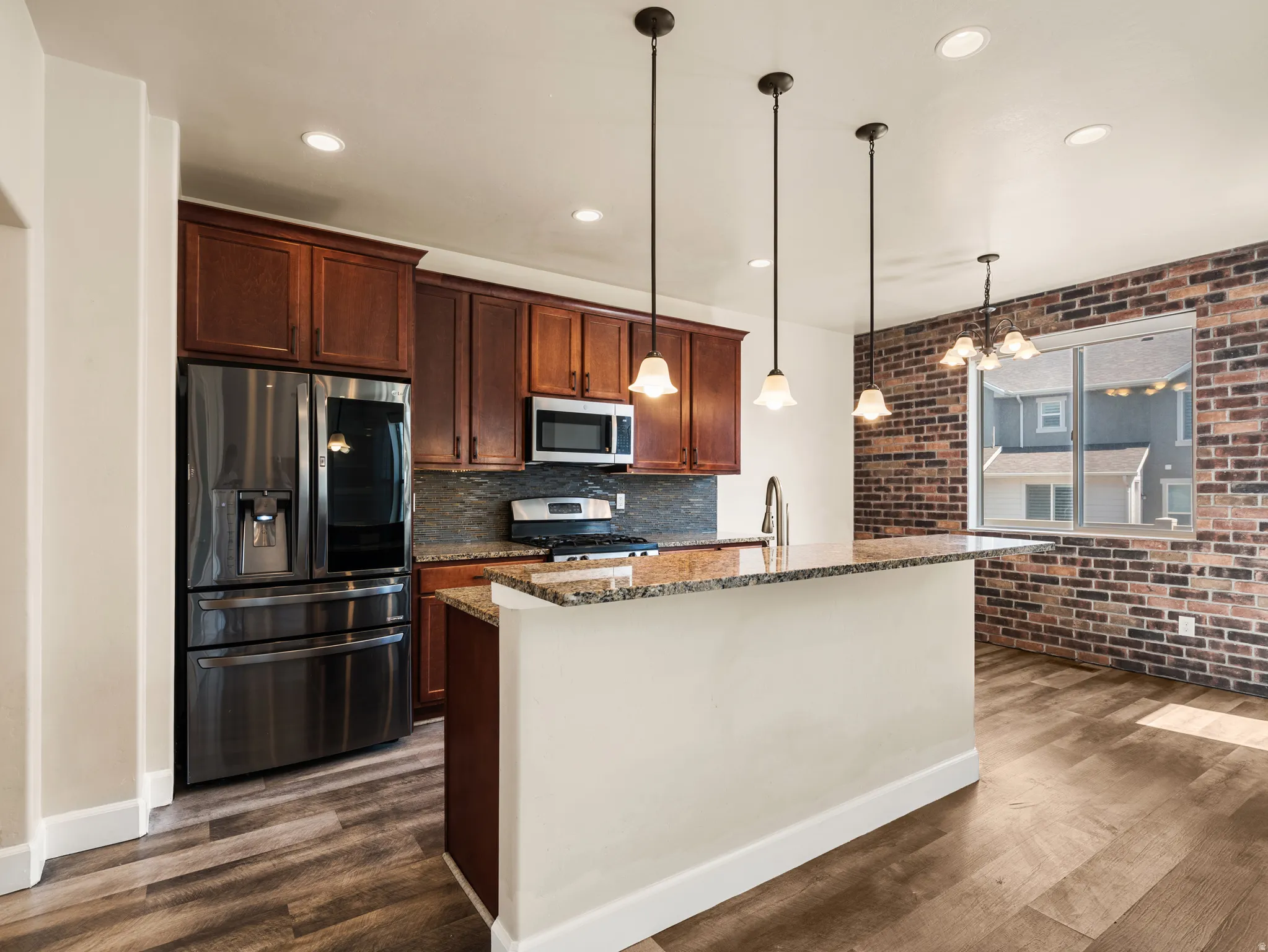 Modern kitchen featuring rich wood cabinetry, stainless steel appliances including a French-door refrigerator and built-in microwave, granite countertops, and a substantial island with pendant lighting