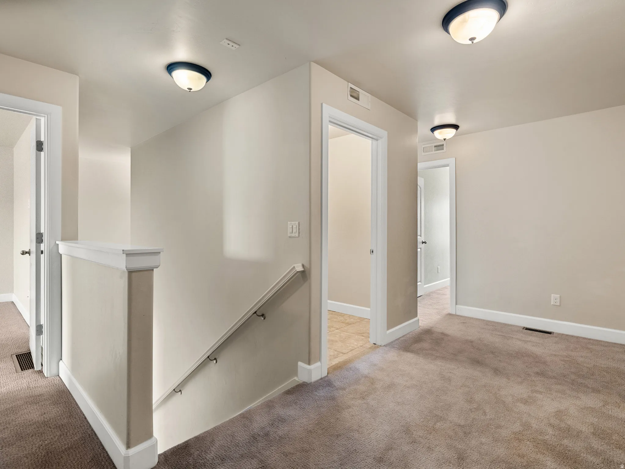 Interior hallway with neutral carpeting, light-toned wall paint, and white trim