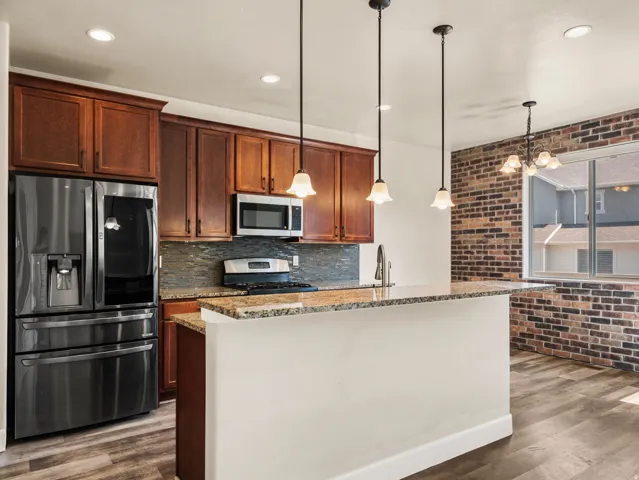 Modern kitchen featuring rich wood cabinetry, stainless steel French-door refrigerator, and granite countertops anchoring a substantial island with pendant lighting