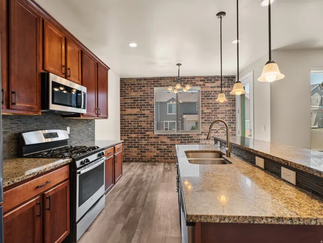 Kitchen featuring rich wood cabinetry, stainless steel appliances, granite countertops, a mosaic tile backsplash, and wood-finish flooring