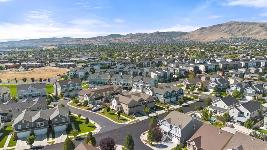 Expansive suburban neighborhood featuring a mix of residential properties, paved streets, and green spaces, all set against a prominent mountain backdrop under a clear blue sky