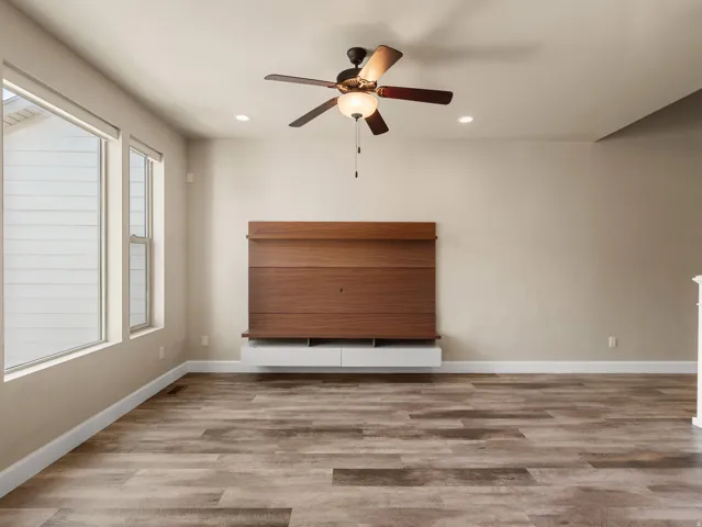 Spacious room featuring wood-finish flooring, a built-in media console with a wood panel accent, and a ceiling fan with integrated lighting