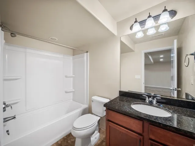 Bathroom featuring a tub/shower combination with integrated shelving, dark wood-finish vanity with a dark speckled countertop, and an undermount sink