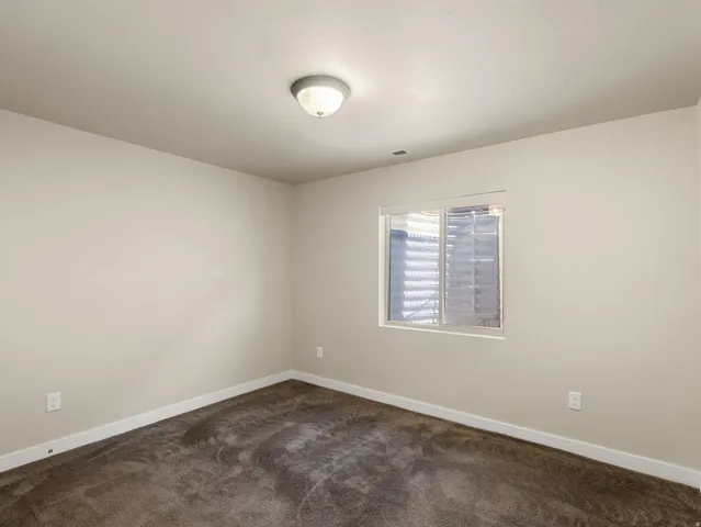Spacious bedroom featuring neutral wall finishes, carpeted flooring, dual wall-mounted outlets, recessed ceiling lighting, and a window with integrated blinds providing natural light