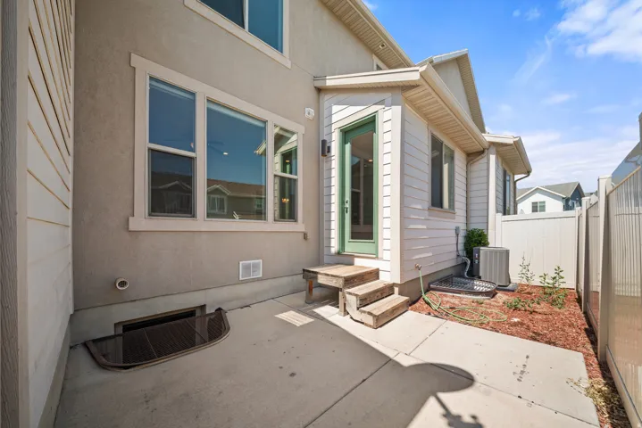 Concrete patio with a basement window well and a side entrance featuring a green door