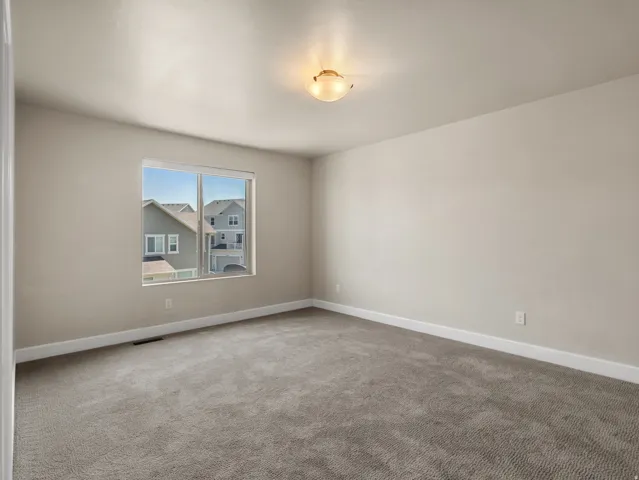 Room featuring neutral wall paint, gray carpeting, white baseboards, and a window with a neighborhood perspective