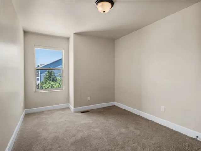 Bright corner bedroom featuring neutral paint finishes, carpet flooring, and abundant natural light from a large window framing mountain scenery