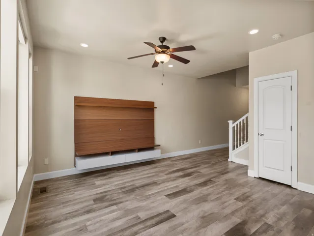 Spacious living area featuring wood-finish flooring, a contemporary built-in media console, and a ceiling fan with integrated lighting