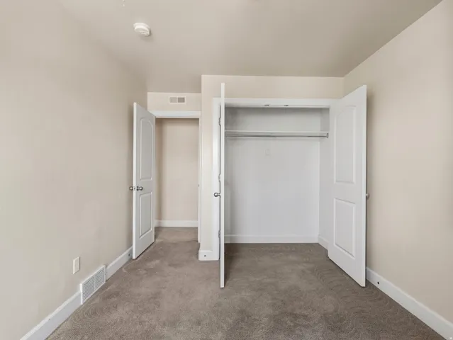 Spacious bedroom featuring neutral wall finishes, neutral-toned carpet flooring, and dual reach-in closets with white-painted doors and interior shelving