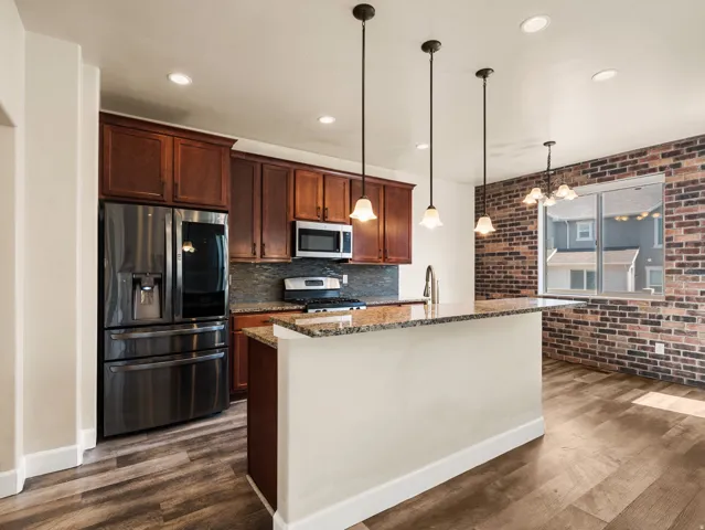 Modern kitchen featuring rich wood cabinetry, stainless steel appliances including a French-door refrigerator and built-in microwave, granite countertops, and a substantial island with pendant lighting