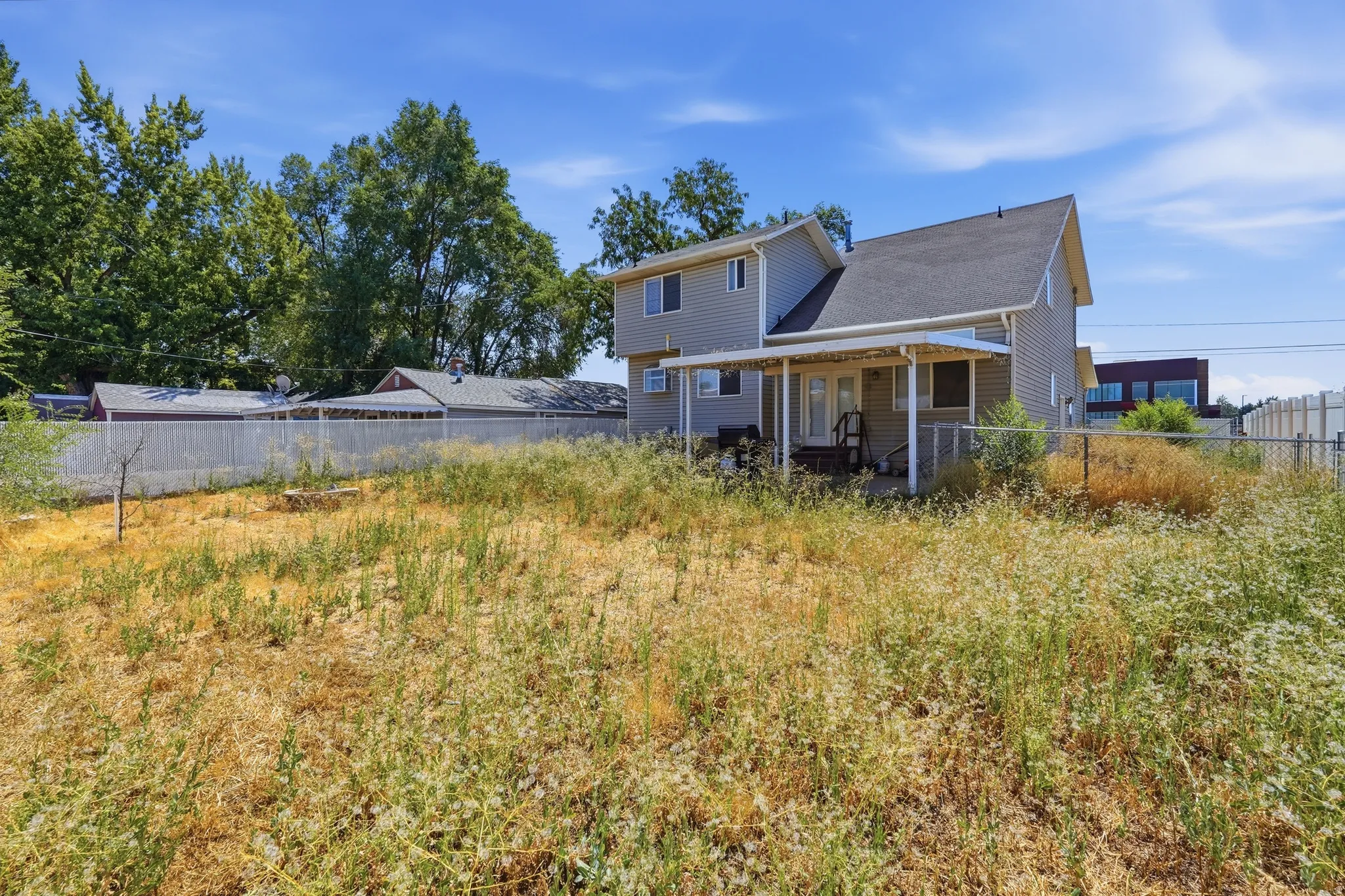 Expansive backyard with chain-link fencing, mature trees, and a covered patio