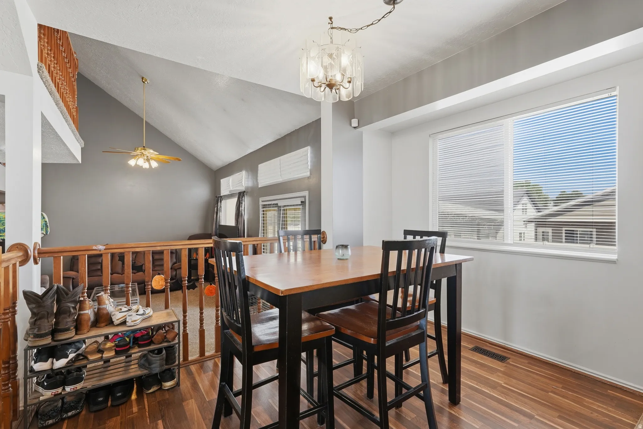 Dining room featuring a black wood-finish table with matching chairs, hardwood flooring, vaulted ceilings with recessed lighting, and expansive windows with cellular shades providing natural light