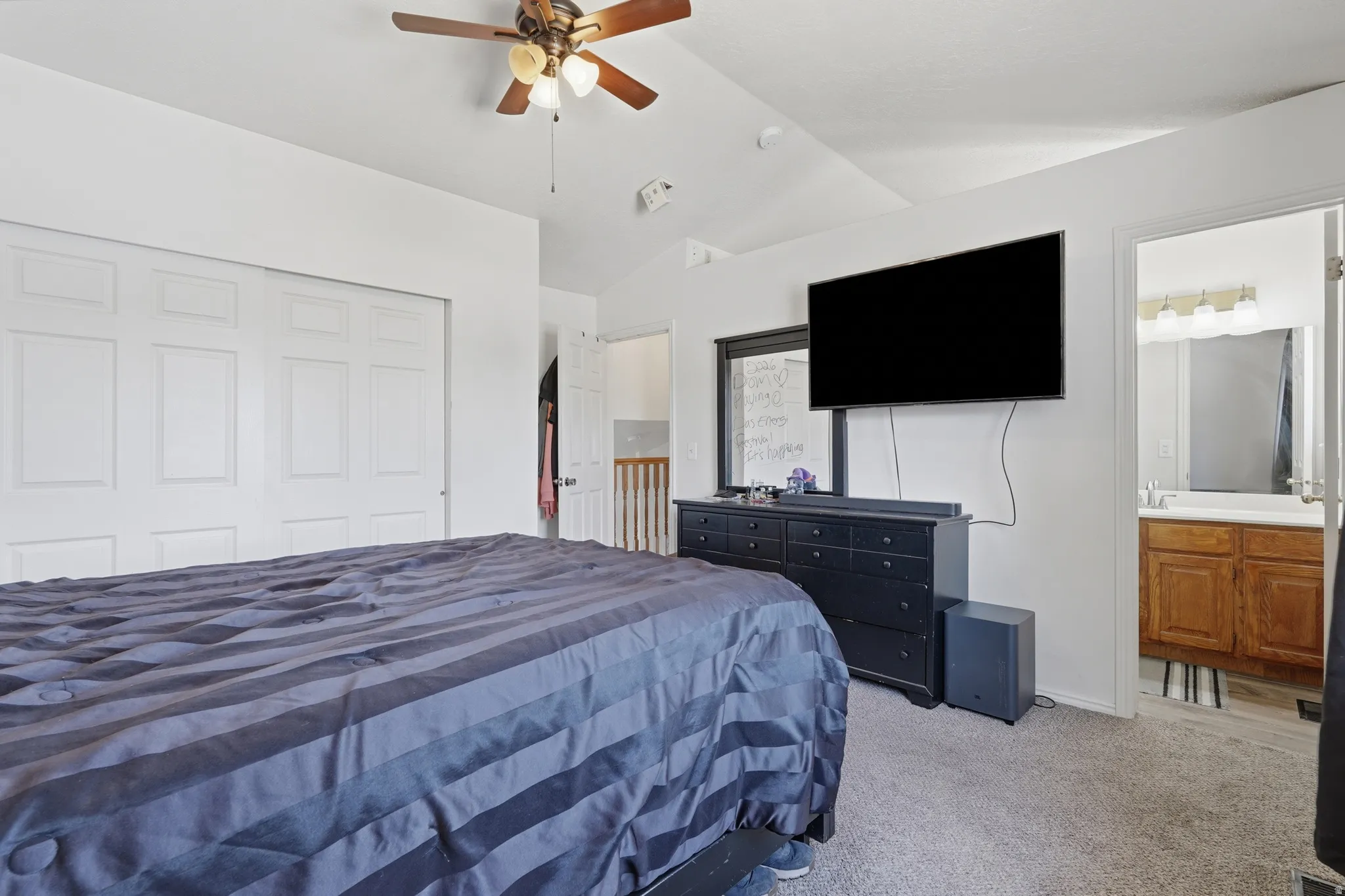 Carpeted bedroom featuring a ceiling fan, bi-fold closet doors, and direct access to a bathroom with a wood-finish vanity