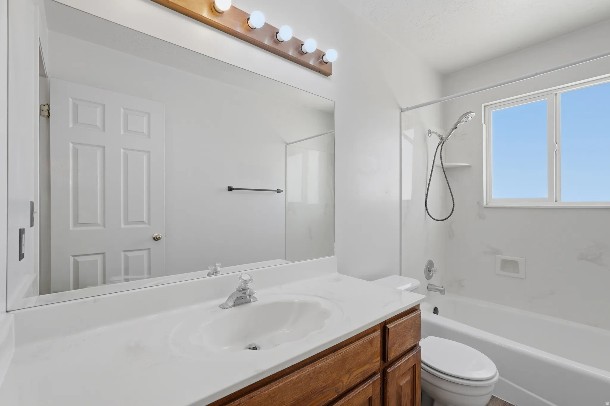 Bright and updated bathroom featuring a spacious white quartz countertop with an undermount sink, wood-finish vanity cabinetry, and a large framed mirror