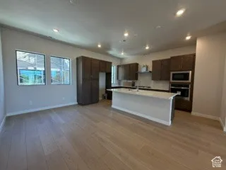 Kitchen featuring dark-toned cabinetry, a central island with a stone-composite countertop, built-in double wall ovens, recessed lighting, and wood-finish flooring
