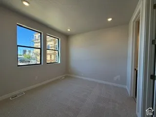 Neutral-toned interior room featuring wall-to-wall carpeting, recessed ceiling lighting, and dual windows with black frames