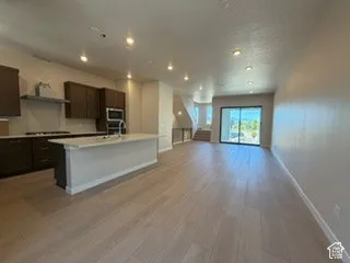 Kitchen featuring dark wood-finish cabinetry, a large central island with light-toned countertops, recessed ceiling lighting, wood-finish flooring, and sliding glass doors