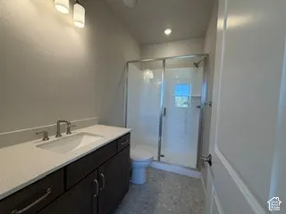 Bathroom featuring a dark wood-finish vanity with a light-toned countertop, integrated basin, walk-in shower with a glass enclosure, and multi-tone tile flooring