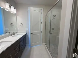 Double vanity with quartz countertops, undermount sinks, full-width mirror, glass-enclosed shower, and tile flooring