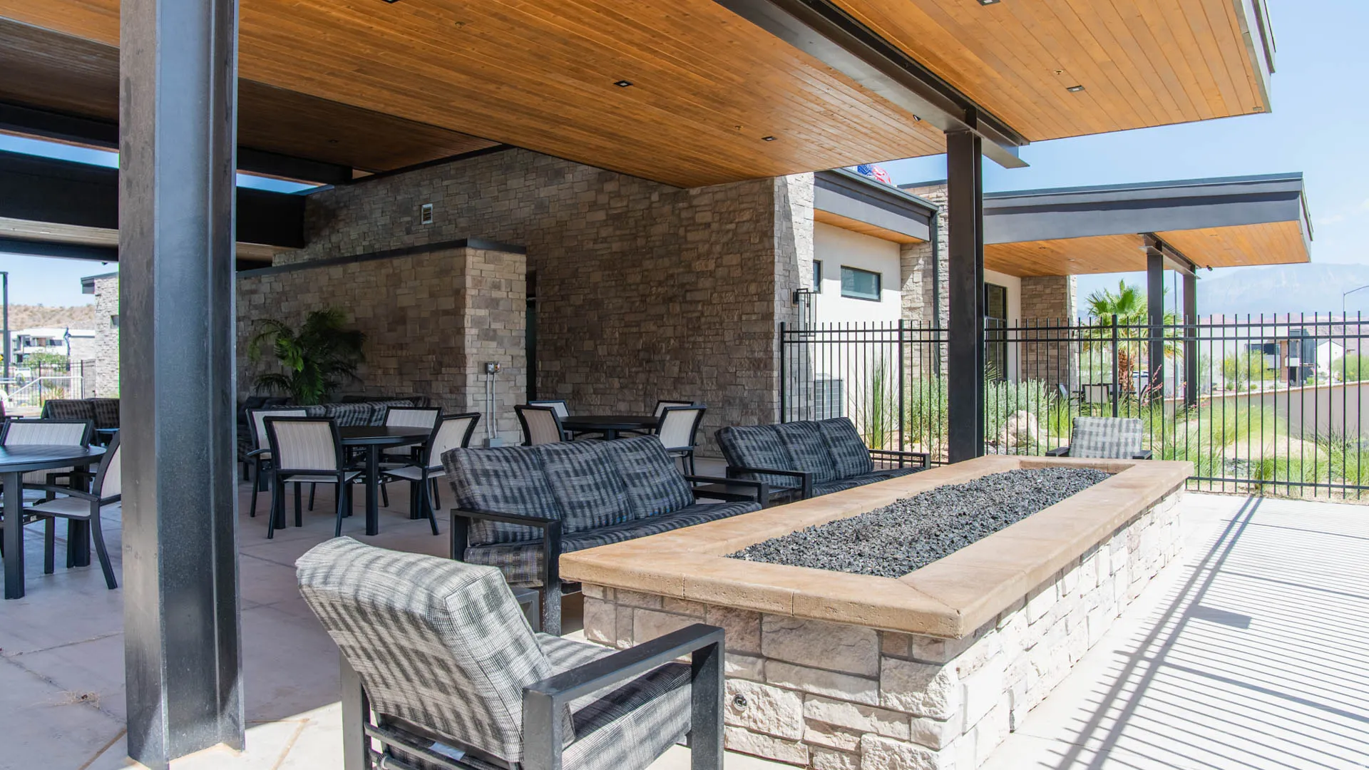 Covered outdoor patio featuring a stone-clad fire pit with dark fire glass, a wood-finish ceiling, and stone veneer walls