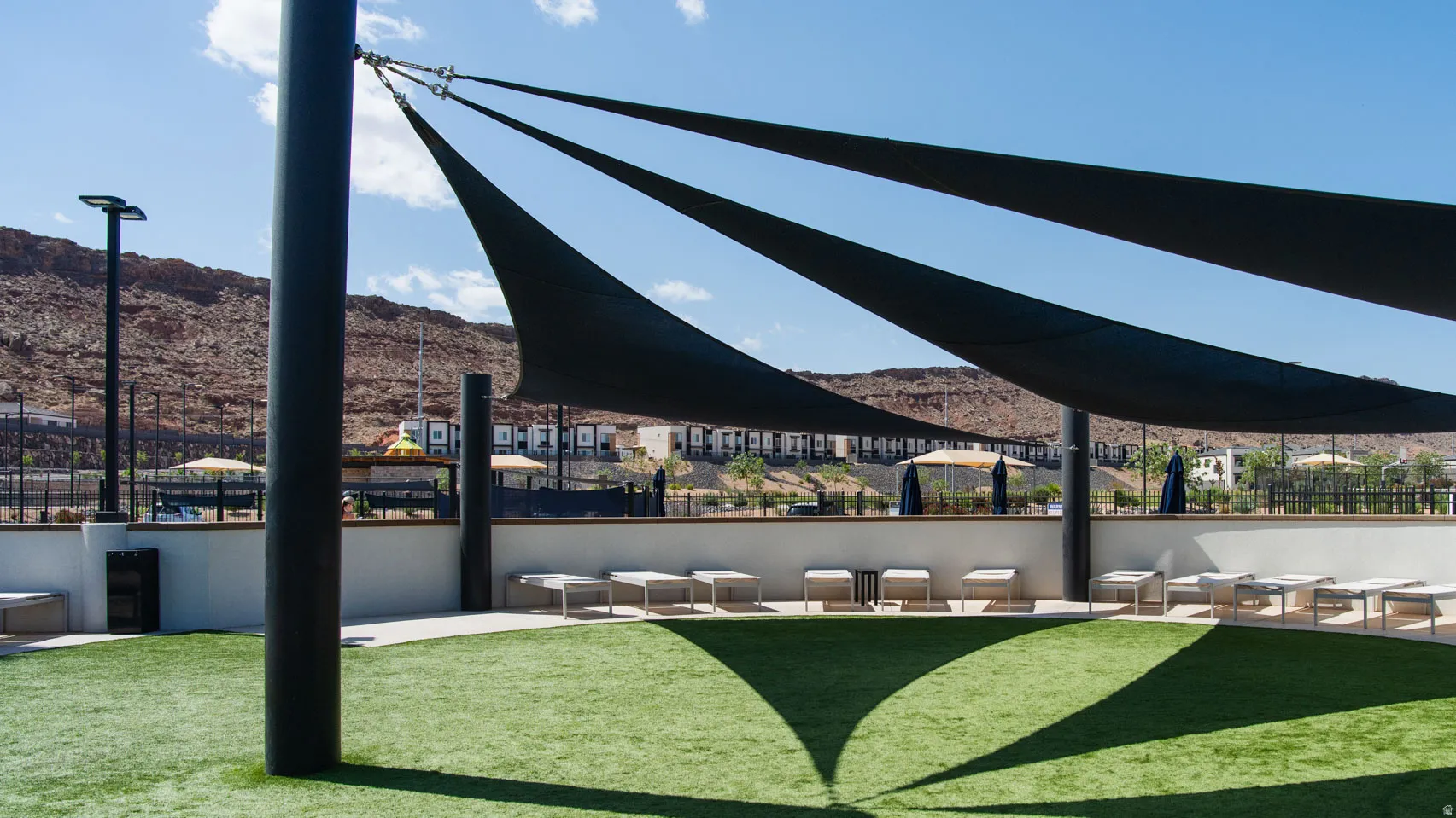 Artificial turf area featuring multiple shade sails, perimeter seating, and desert mountain backdrop