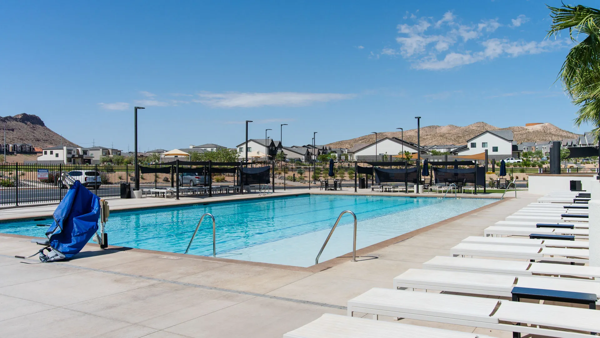 Expansive community pool with a surrounding concrete deck, multiple lounge chairs, and shaded seating areas