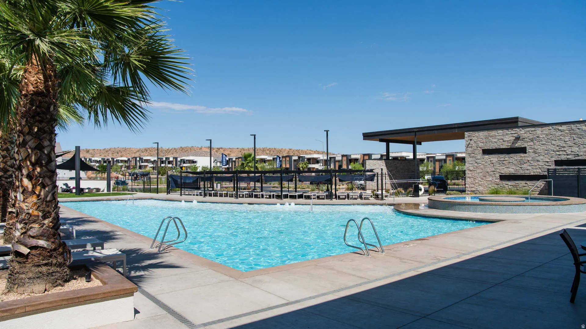 Community swimming pool featuring a connected spa, stone-clad clubhouse, covered lounge area, and desert landscaping