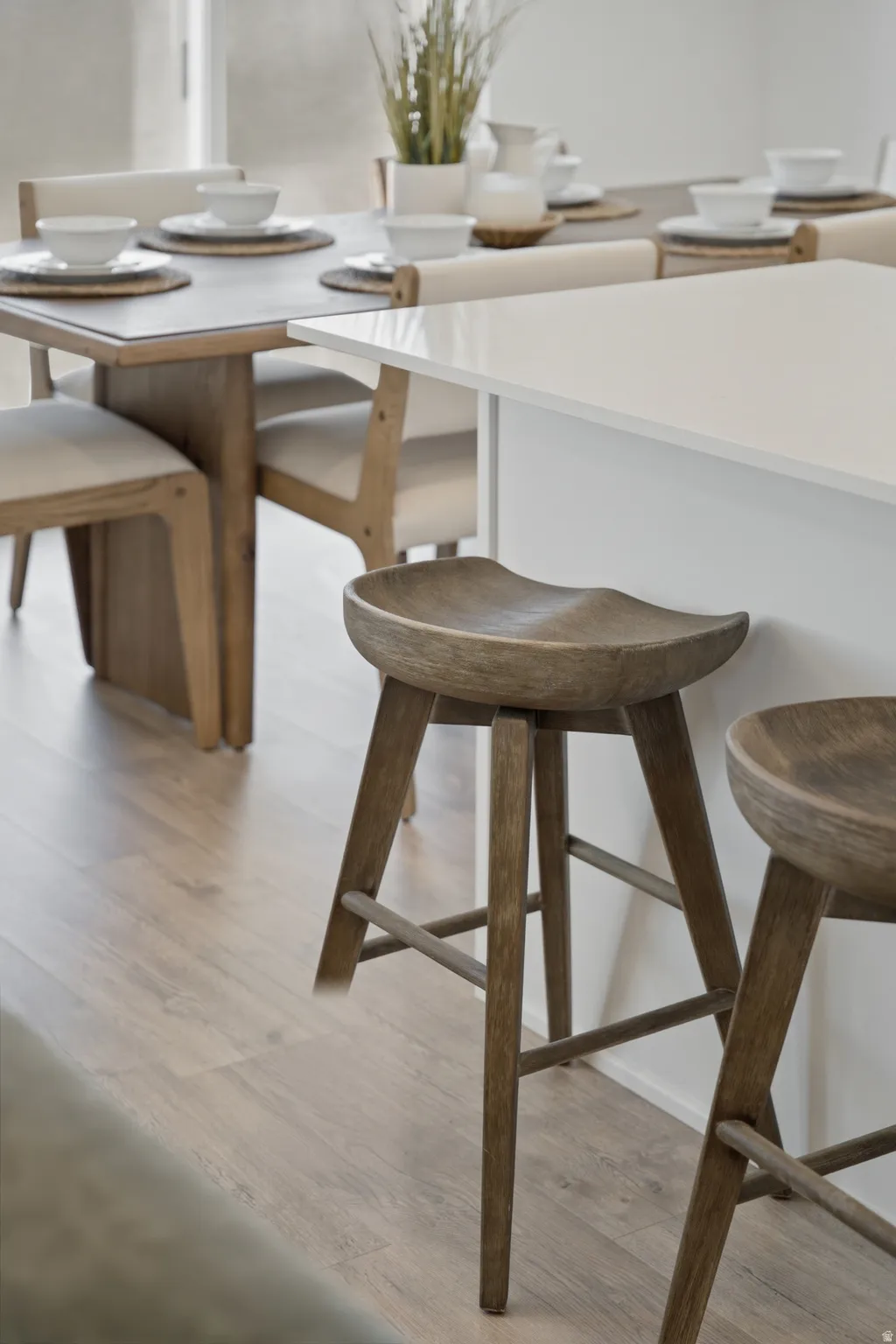 Modern dining space featuring a white quartz countertop island with waterfall edge, natural wood-finish bar seating with sculptural turned-leg stools, and light wood-finish flooring throughout