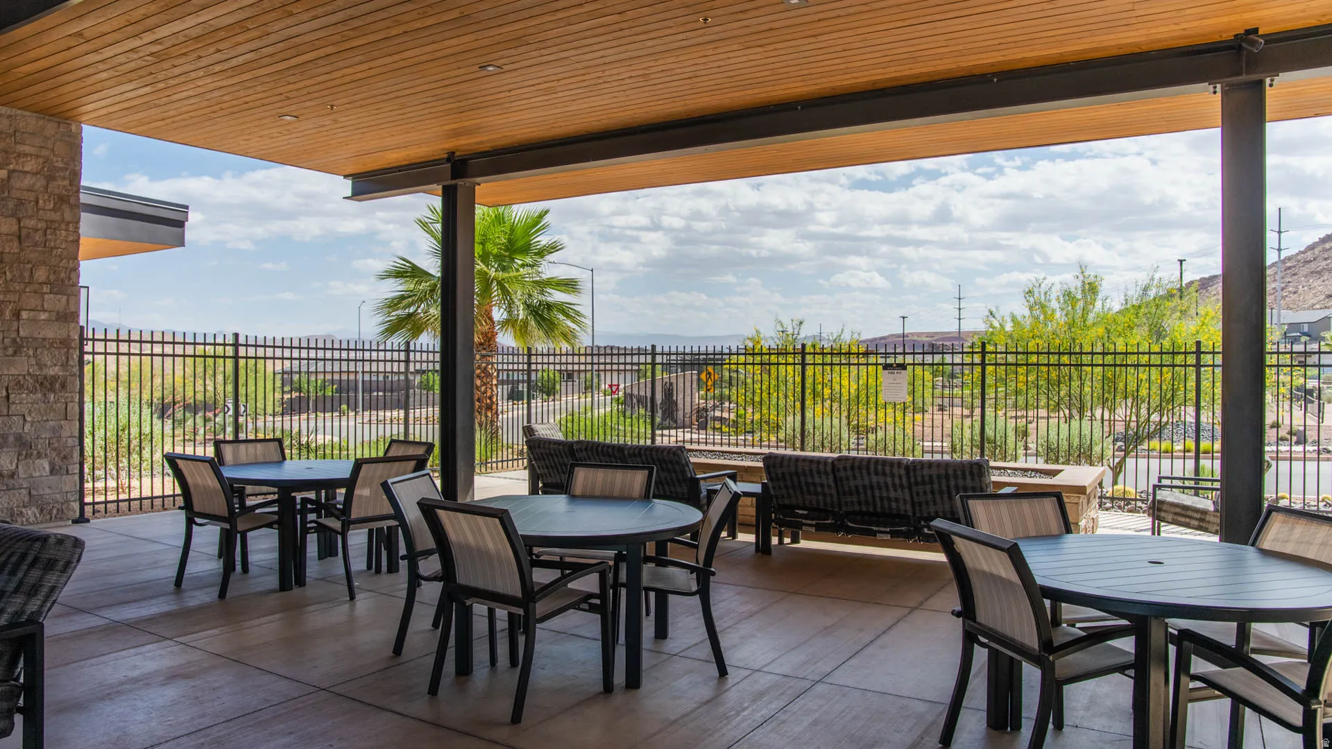 Expansive outdoor patio featuring a wood-finish ceiling, stone accent wall, concrete flooring, and metal fencing