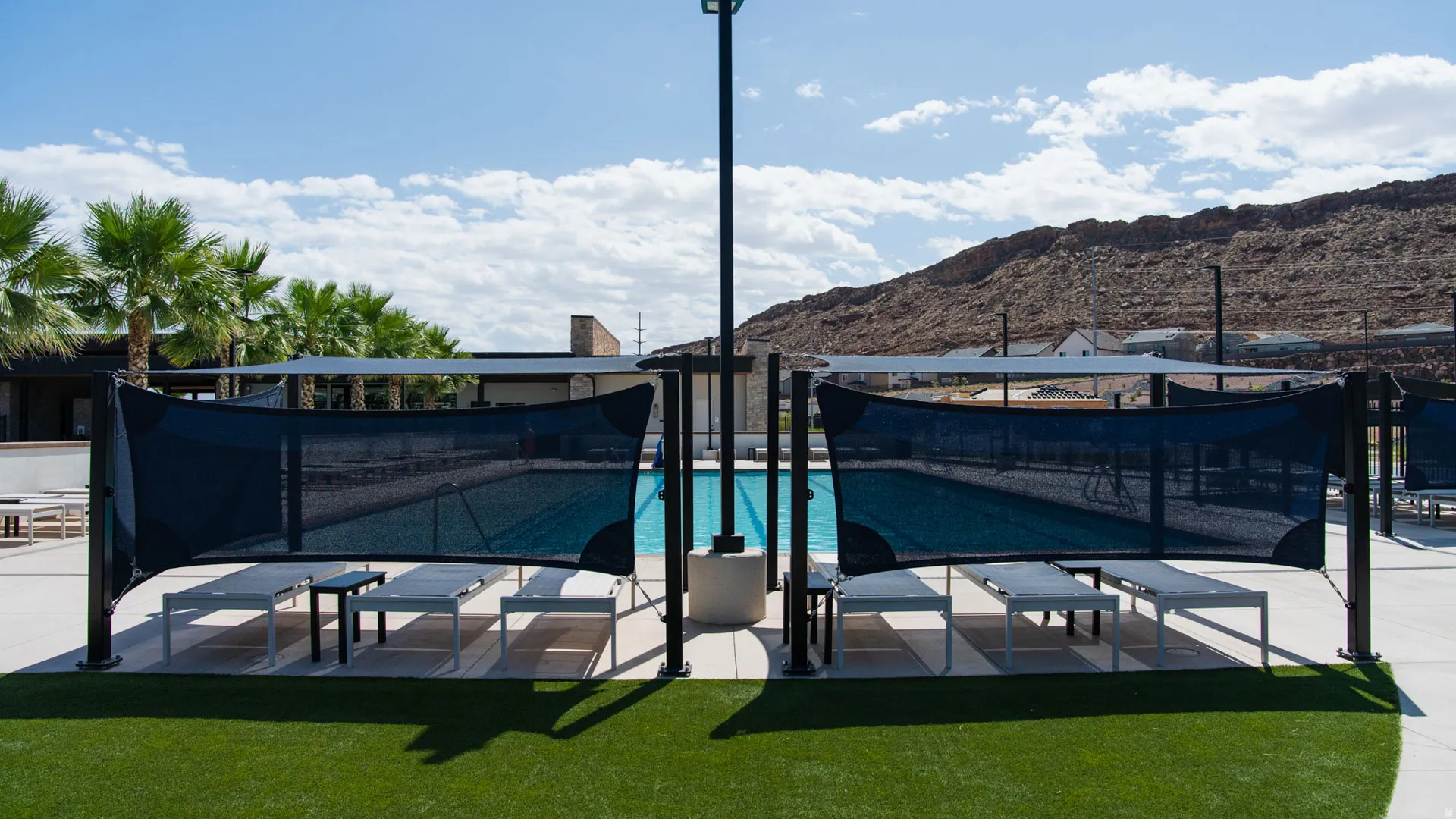 Resort-style pool area featuring a rectangular pool, shade structures, lounge seating, and artificial turf surrounds