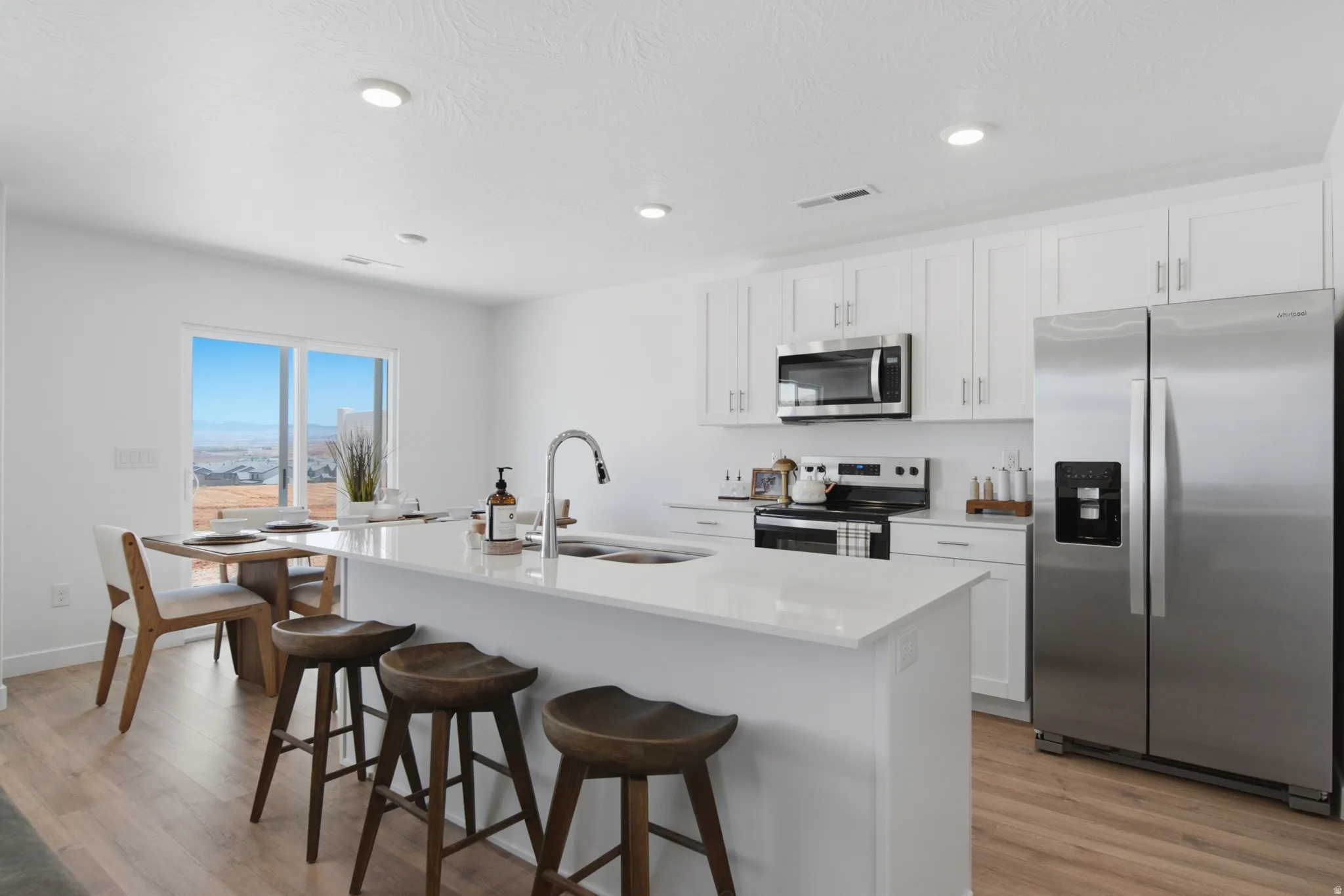 Modern kitchen featuring white cabinetry, stainless steel appliances including a side-by-side refrigerator and microwave, and a waterfall-edge white quartz island with seating for three