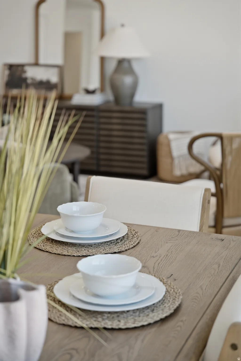 Elegant dining area showcasing a light wood-finish table with natural fiber place mats, white ceramic dinnerware, and woven seating