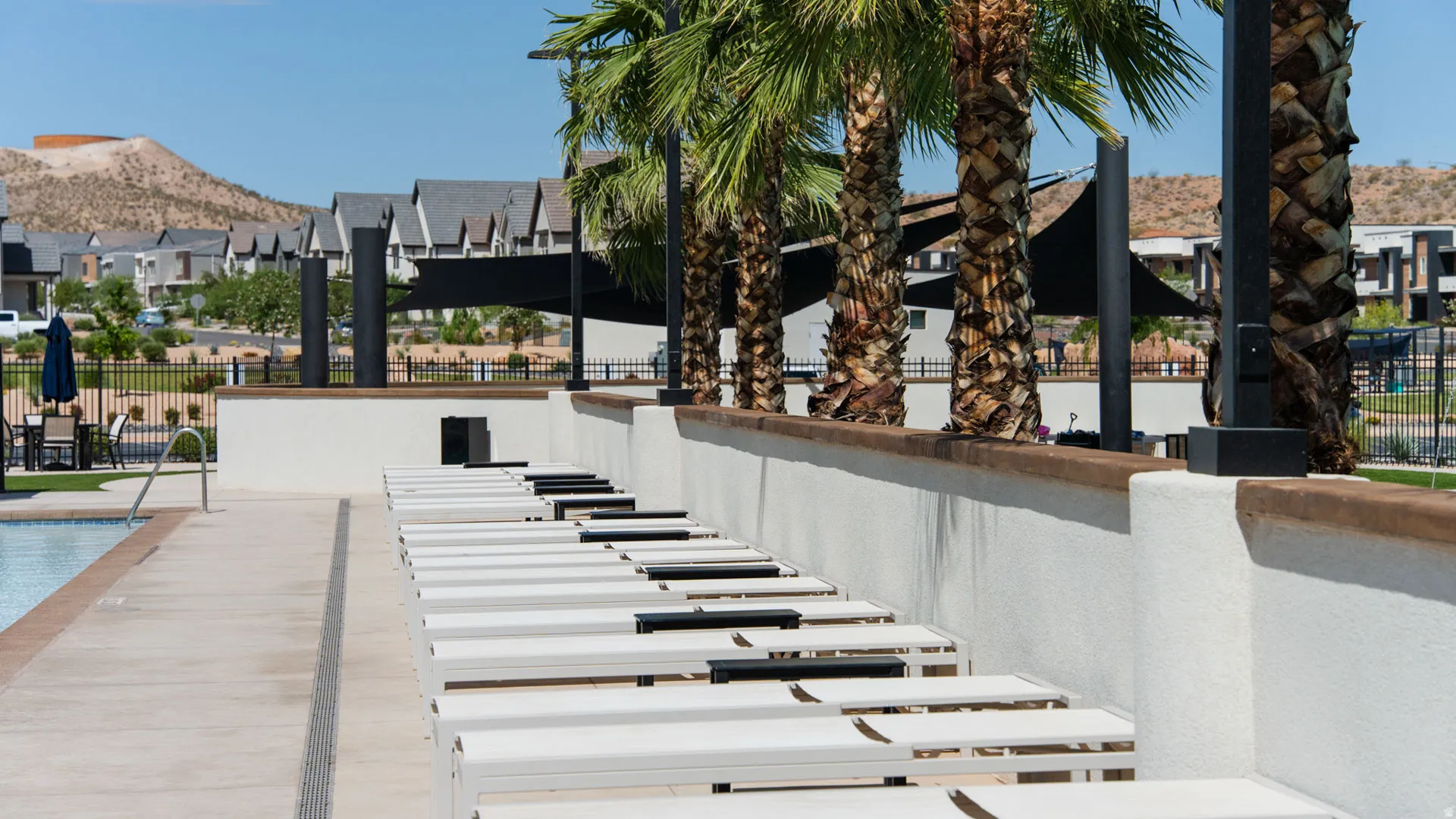 Poolside lounge area featuring multiple chaise lounges, a concrete pool deck, and a perimeter wall