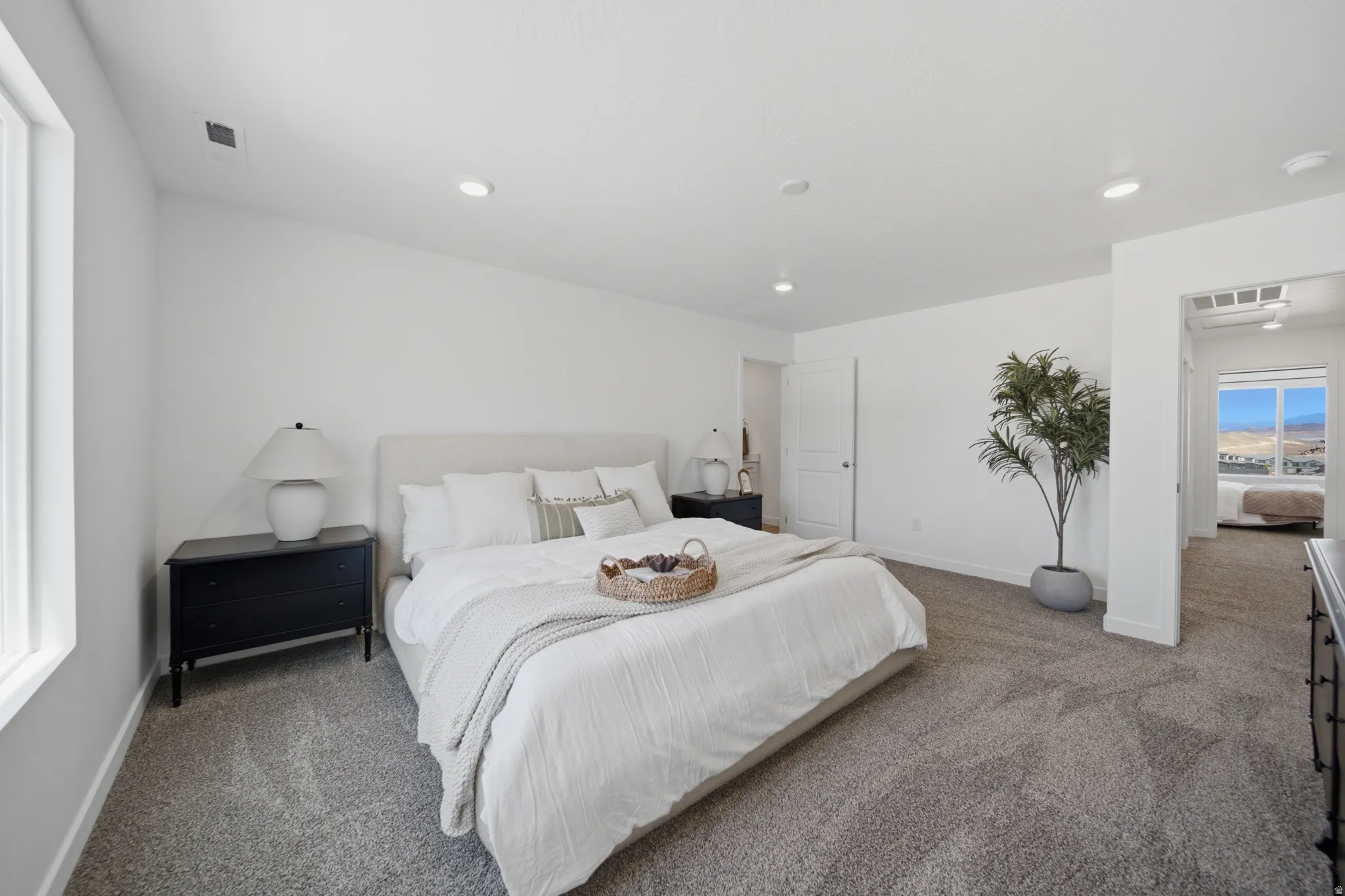 Spacious primary bedroom featuring a neutral color palette, carpeted flooring, recessed lighting throughout, and large windows providing natural light