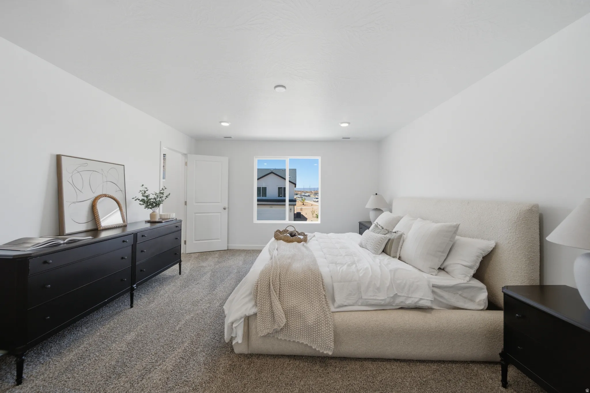 Spacious primary bedroom featuring a neutral upholstered bed frame, recessed ceiling lighting, gray carpet flooring, and abundant natural light from sliding glass doors