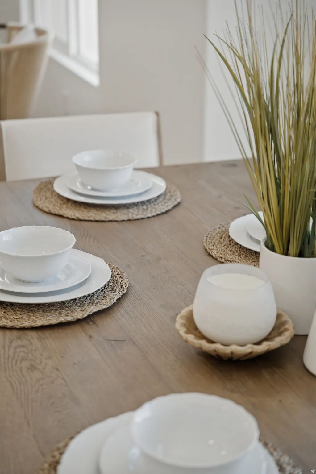 Elegant dining table featuring wood-finish flooring, natural woven placemats, and clean white dinnerware