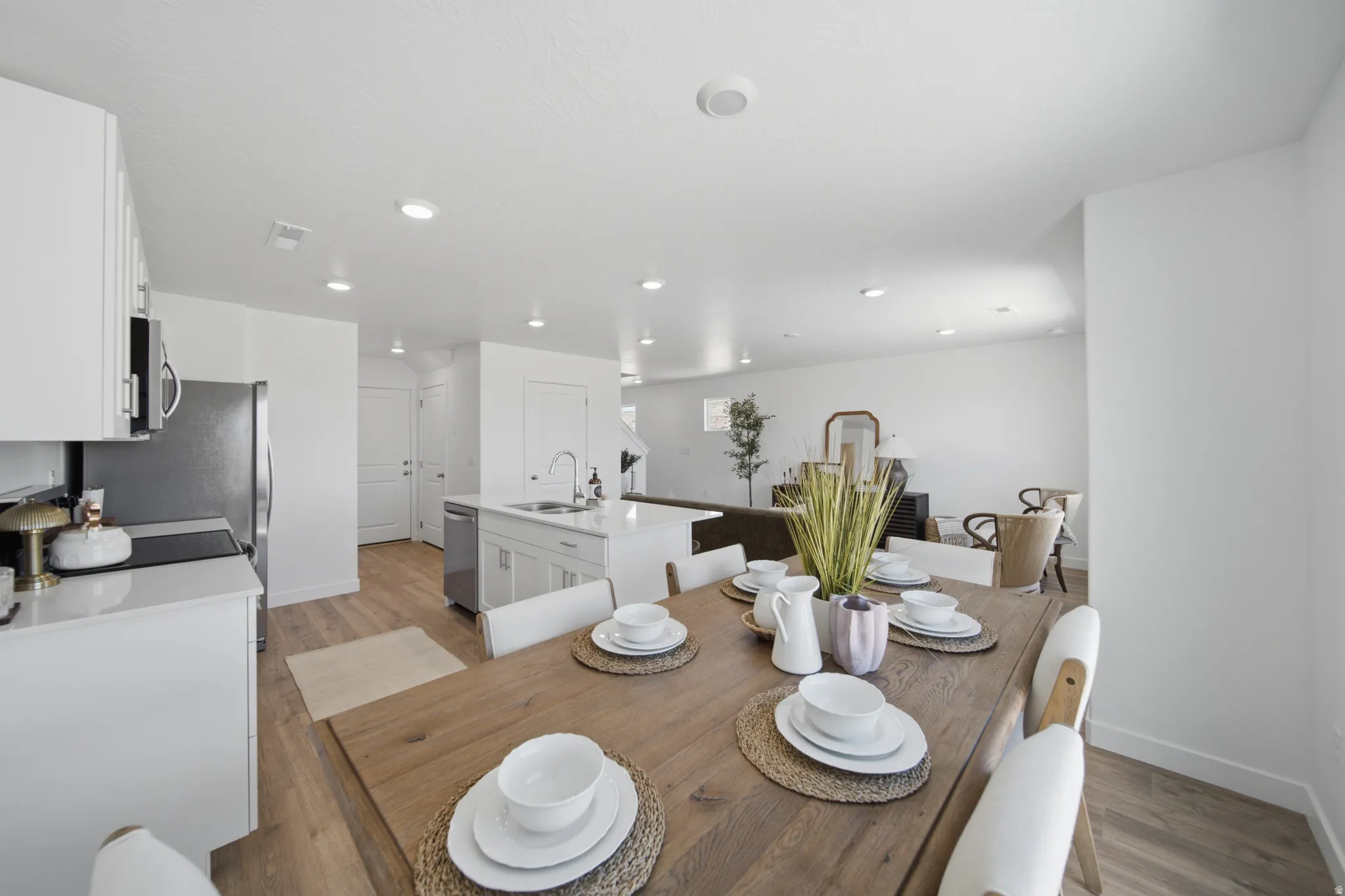 Open-concept living space with wood-finish flooring, white cabinetry, recessed lighting, a kitchen island with sink, and stainless steel appliances