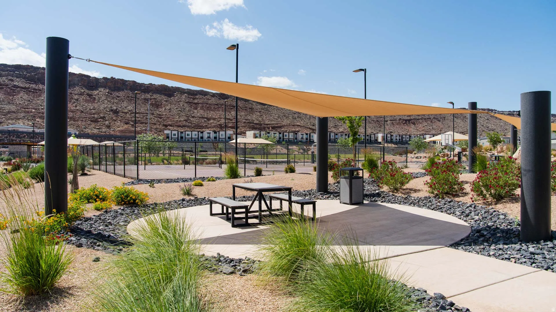 Outdoor recreation area featuring a shade sail, concrete patio with picnic table, and surrounding desert landscaping with decorative rock
