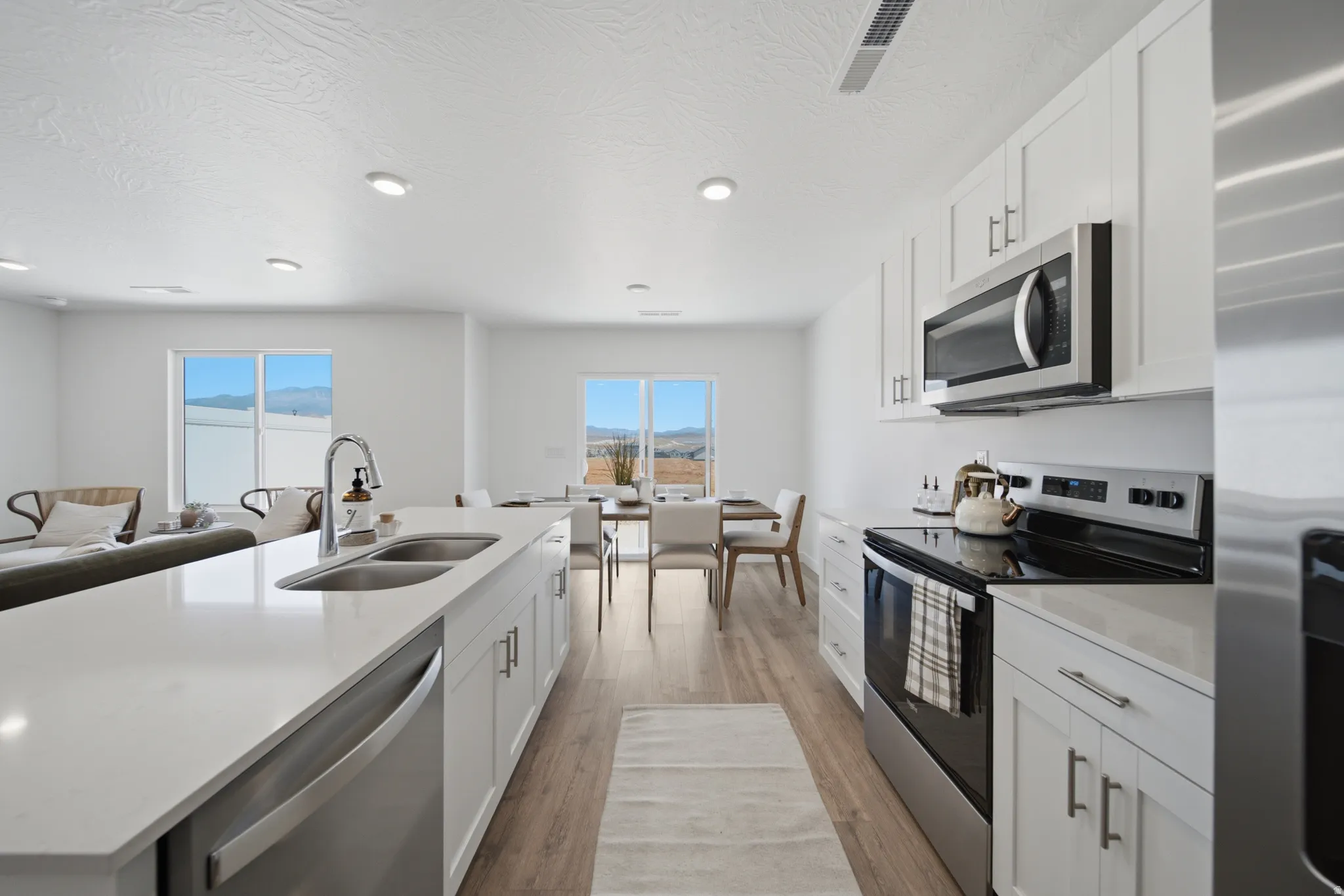 Open-concept kitchen featuring white cabinetry, stainless steel appliances, a large island with a double sink, and wood-finish flooring