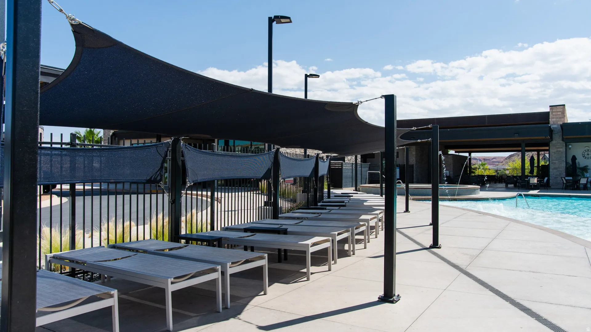 Poolside lounge area featuring a curved swimming pool, a shaded patio with multiple lounge chairs, and an adjacent structure with stone accents