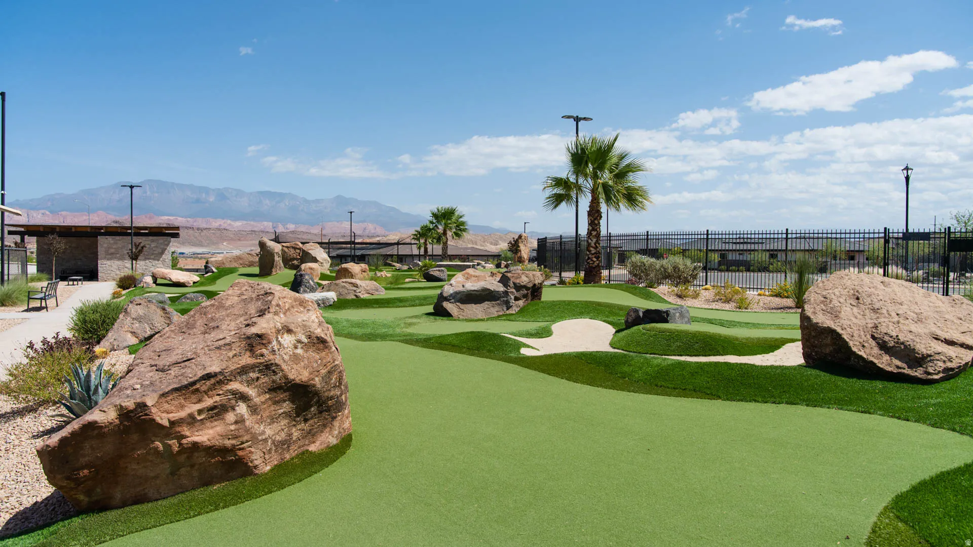Putting green featuring artificial turf, integrated sand traps, and natural rock landscaping