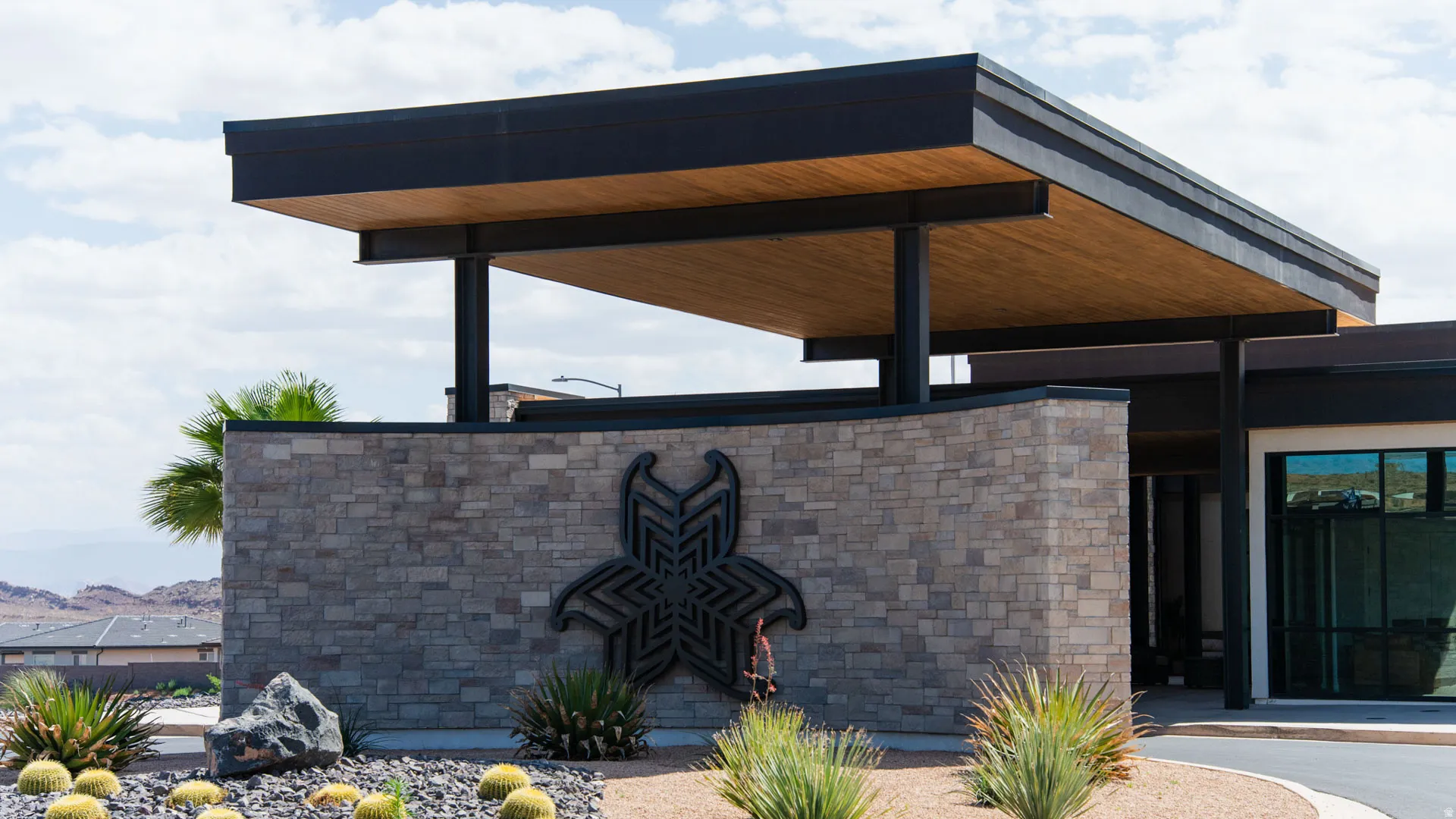Modern architectural entrance featuring a stone-clad wall and an expansive wood-paneled overhang supported by dark structural beams