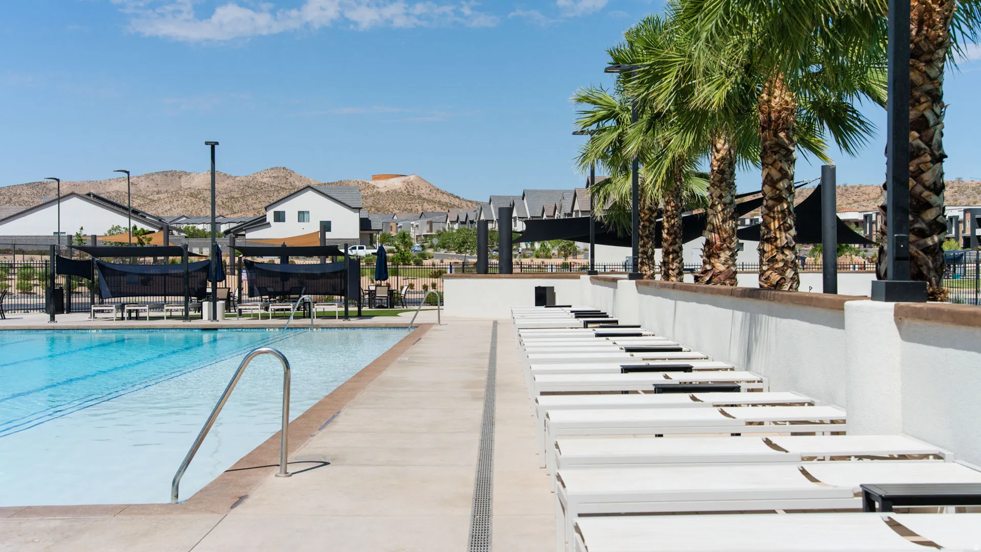 Resort-style community pool and spa area featuring Olympic-length lap lanes, sun loungers, mature palm trees, and mountain vistas