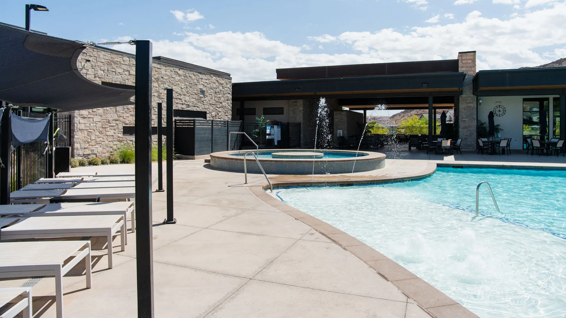 Resort-style pool and spa area featuring crystal-clear waters, spacious sun deck with lounge seating, modern pergola-covered pavilion with integrated shade structures, stone accent walls, and professional-grade hardscaping throughout the expansive outdoor